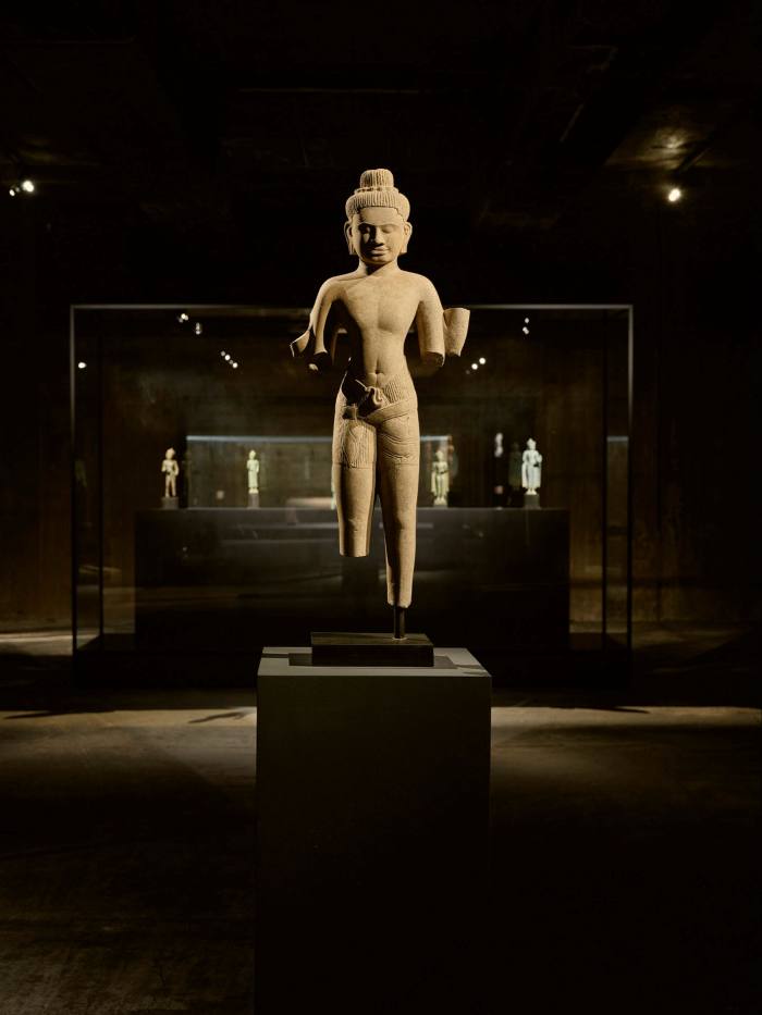 A golden stone statue of a man with a thin waist and pointed hat