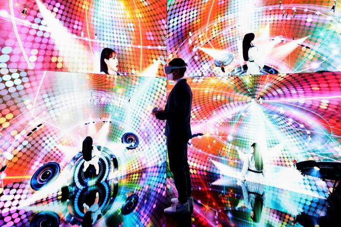 A man in a virtual reality headset stands between kaleidoscopic, vibrantly colored screens