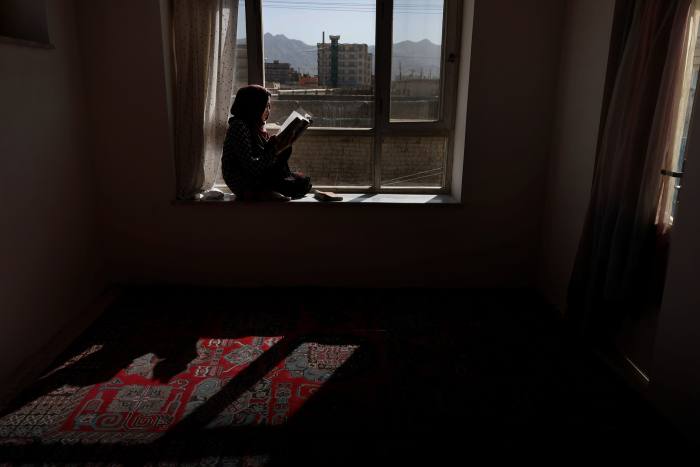 A girl in Kabul reads a book beside a window