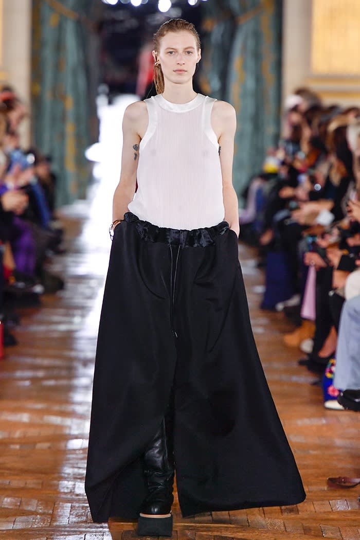 A female model walks down the catwalk in a white sleeveless top and long, wide black skirt