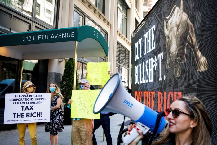 People protest on a New York street, holding signs with slogans such as 'Tax the Rich'