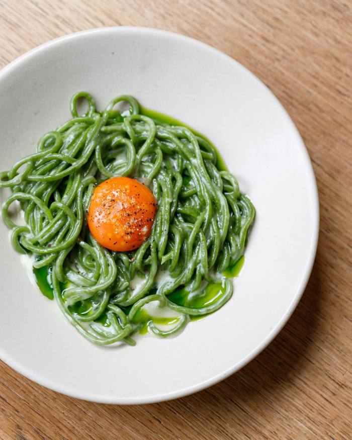 A bowl of fluorescent-green wild garlic chitarra spaghetti, with an egg yolk nested in the middle