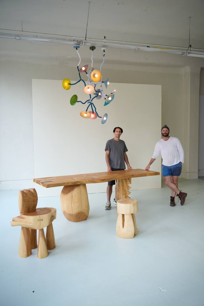 A long wooden table and chairs with the maker, Vince Skelly, and his gallery owner Alex Tieghi-Walker