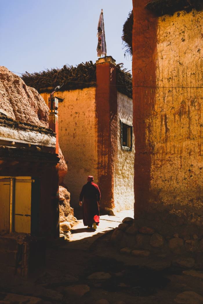 A monk walks towards two saffron-coloured buildings 