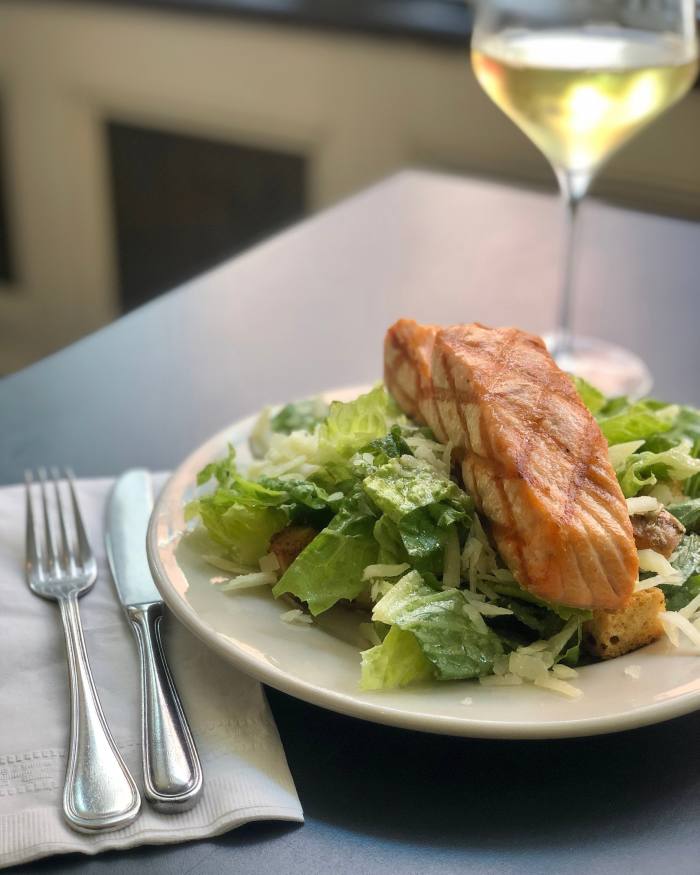 Un plato de ensalada César con salmón en Estancia 460, con cuchillo y tenedor a su izquierda