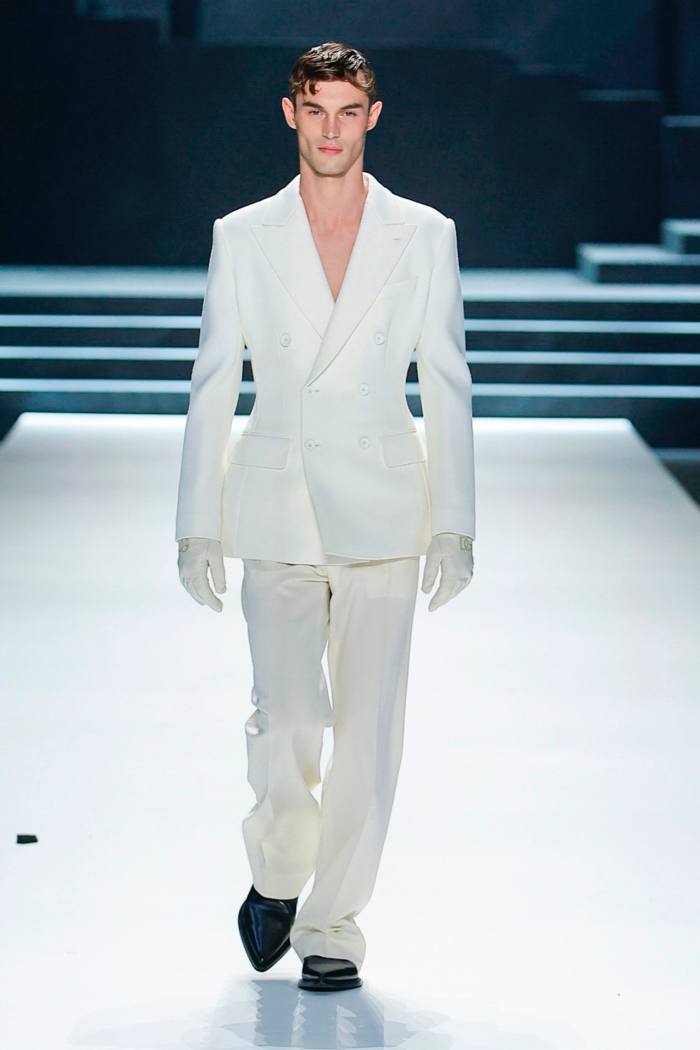 A model in a white suit walks the runway