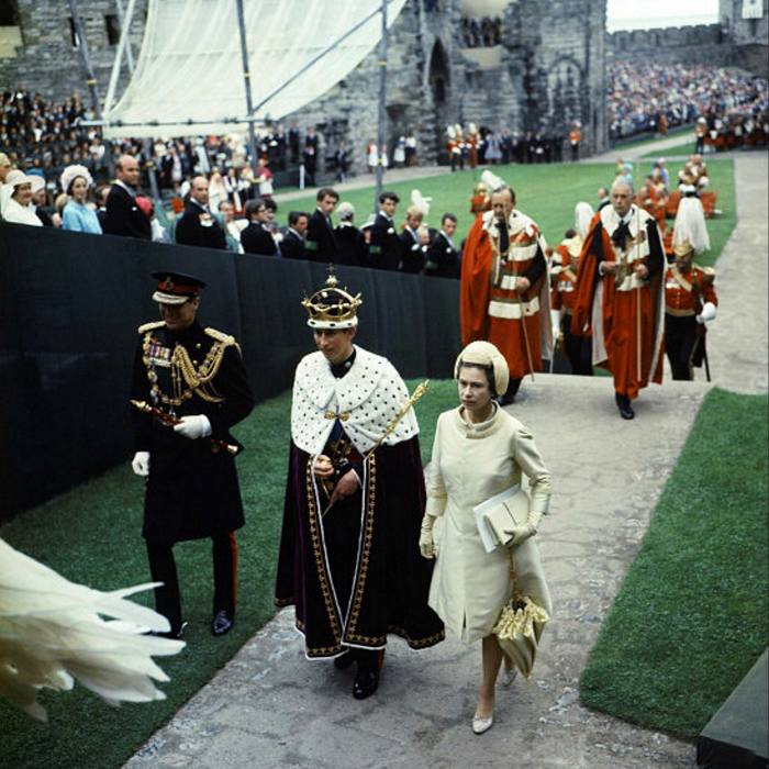 The Queen and the Prince of Wales walking in process in Caernarfon Castle, while people in ceremonial dress follow them