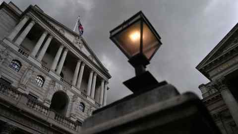 Foto con vistas a la fachada del Banco de Inglaterra al atardecer con una farola en primer plano y un cielo sombrío detrás