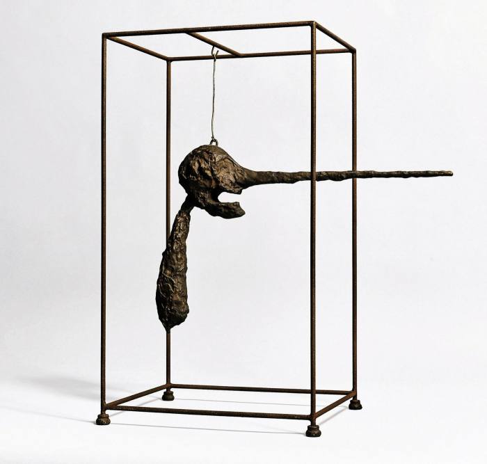 A bronze etiolated human head with an extremely long straight nose hangs in a bronze cage