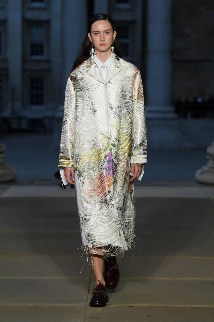A female catwalk model in a mother-of-pearl effect white coat with shimmery colours 
