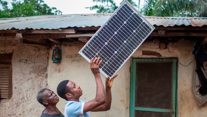 A Ghanaian farmer holds up a solar panel, watched by his sceptical mother