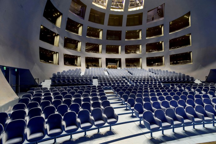 A spherical auditorium with rows of blue seats and boxes carved into the curved concrete wall