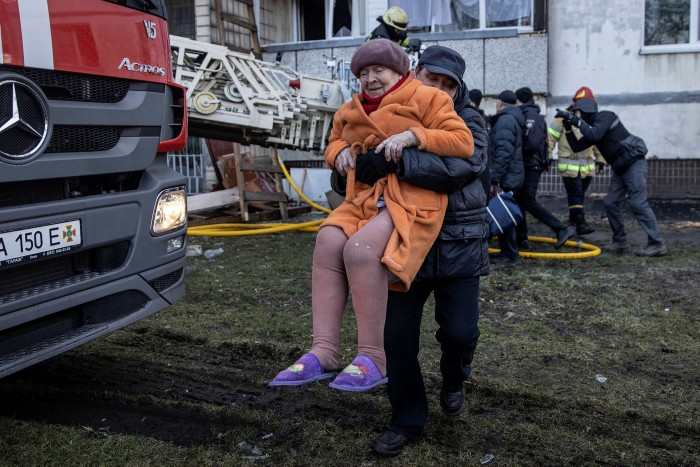 An elderly woman is carried by a rescuer from a building