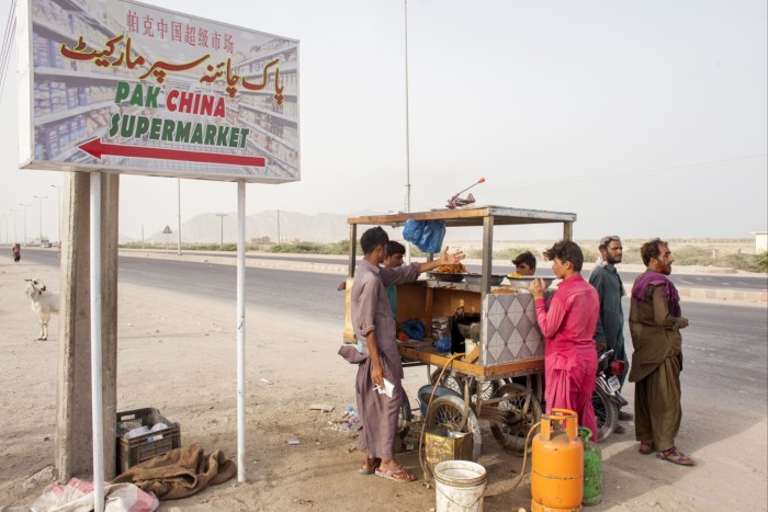 A street food vendor serves customers next to a sign for a Pak China supermarket in Gwadar, Balochistan, Pakistan