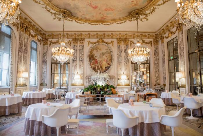 Circular tables and chairs in a large stately room with mirrors, chandeliers and an ornate painting
