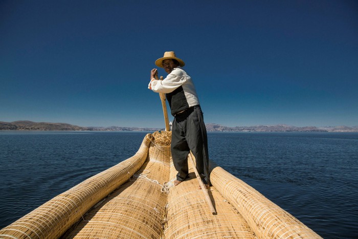 a man standing on the stern of a boat made of reeds