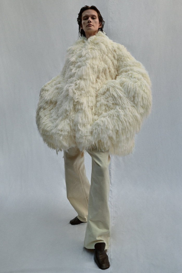 A model in white trousers and a white coat of shaggy fabric resembling ostrich feathers