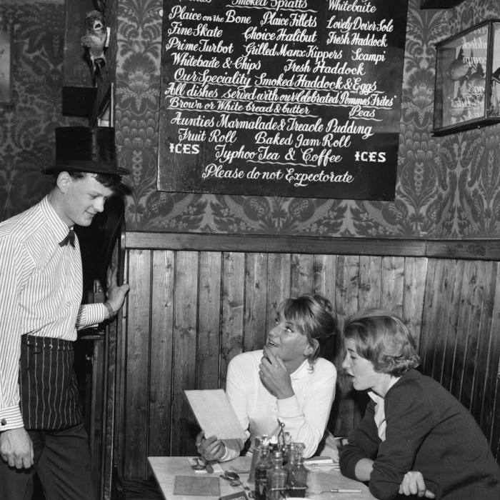 A waiter serves two women sat at a table in a London restaurant in 1962