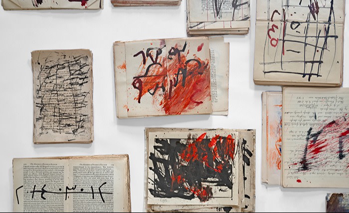 An art installation featuring several books with their pages open and adorned with expressive black and red strokes