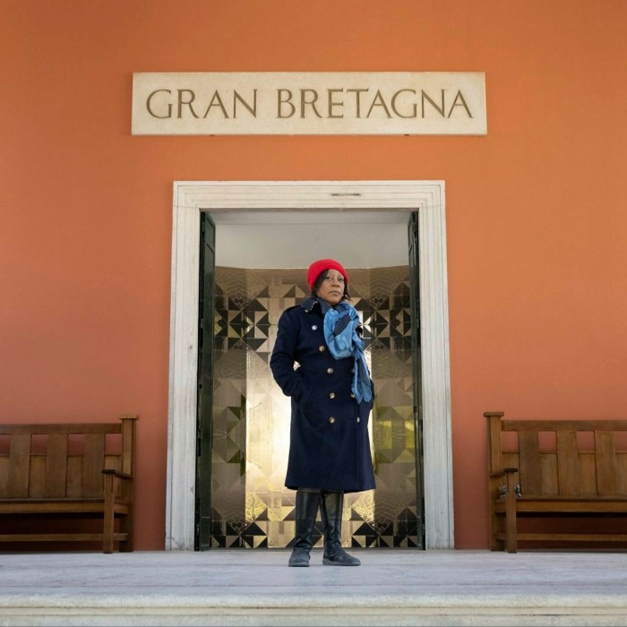 A woman in a navy blue coat stands outside the entrance to the pavilion, above which a sign reads ‘Gran Bretagna’