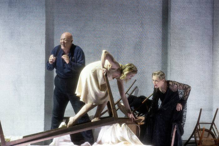 A woman in a white nightgown climbs an overturned table as a woman watches in horror and a man in joy