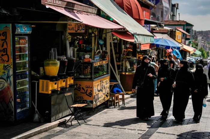 Women walk past a Syrian restaurant in an outdoor market in Fatih district of Istanbul
