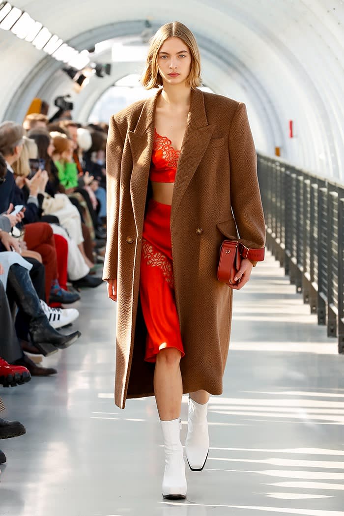 A female model wears a red lace bra and underwear beneath a long coat