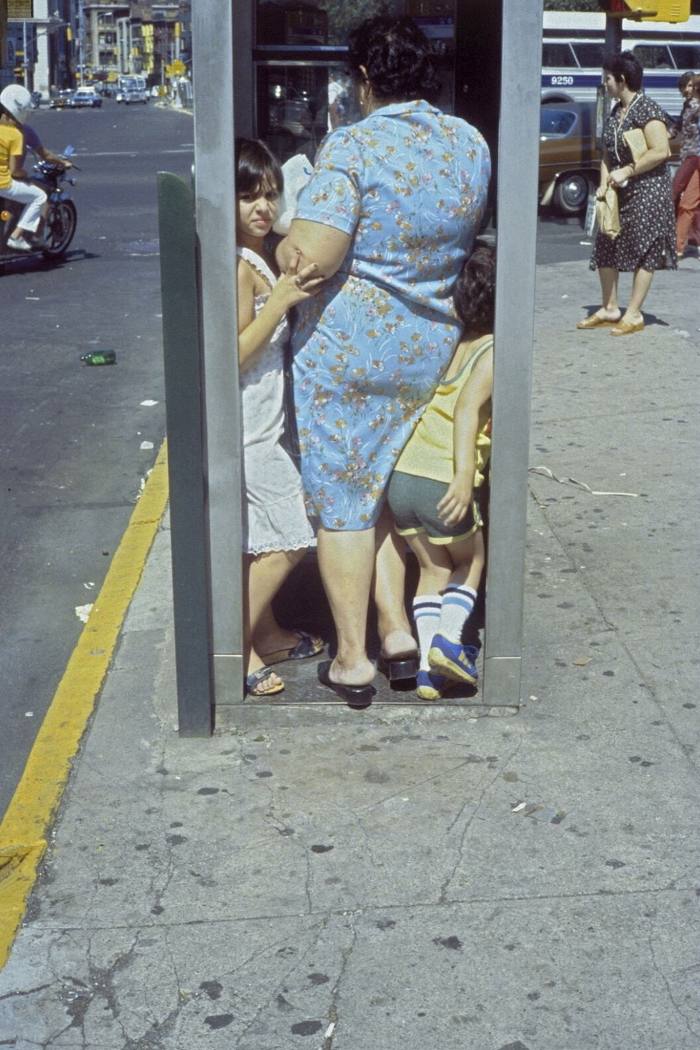 A plump woman and two children squashed into a phone booth
