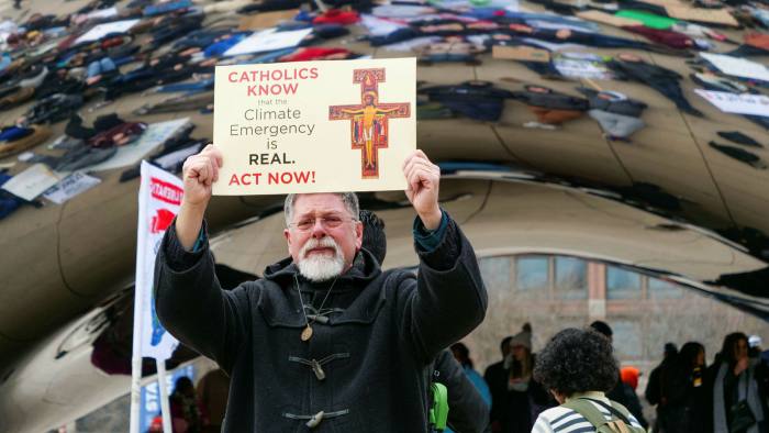 A man holds a sign stating Catholics know climate emergency is real sign at the climate change protest in Millennium park