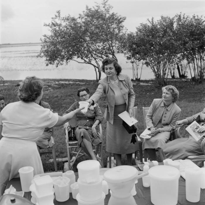 A table of plastic containers with women sitting on fold-out chairs