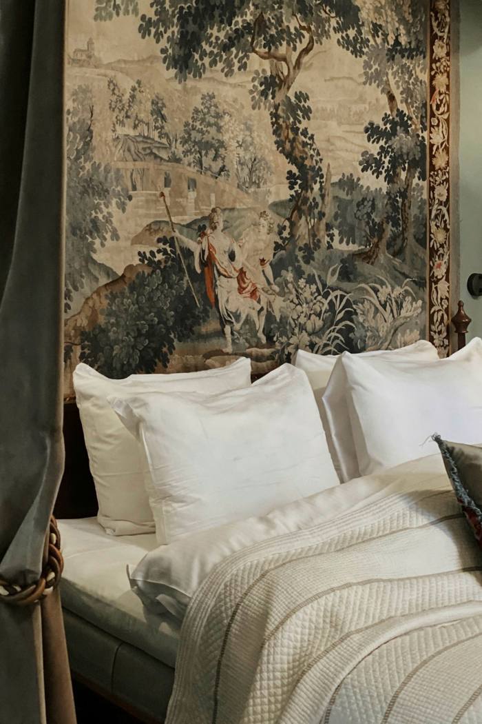 A bed with four large pillows, bedspread and a tapestry for a headboard