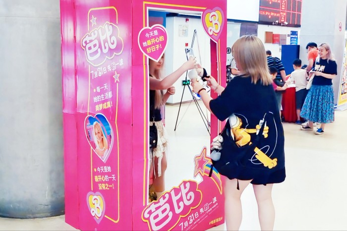 A young woman takes a selfie photograph while standing inside a pink promotional booth