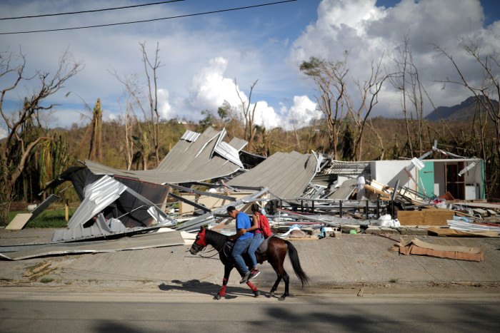 Two people on a horse ride past a house flattened by Hurricane Maria in Puerto Rico
