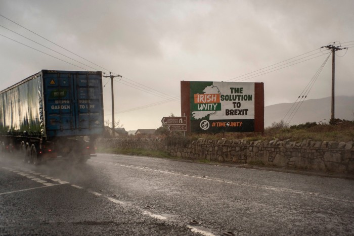 A lorry drives on a wet road, past a sign reading 'Irish Unity: The Solution to Brexit'