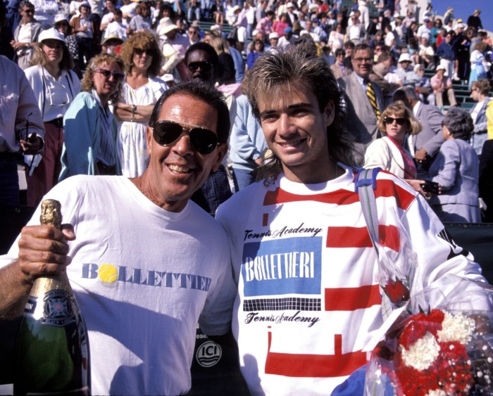 Nick Bollettieri and Andre Agassi pose for a photo with a crowd of tennis spectators in the background