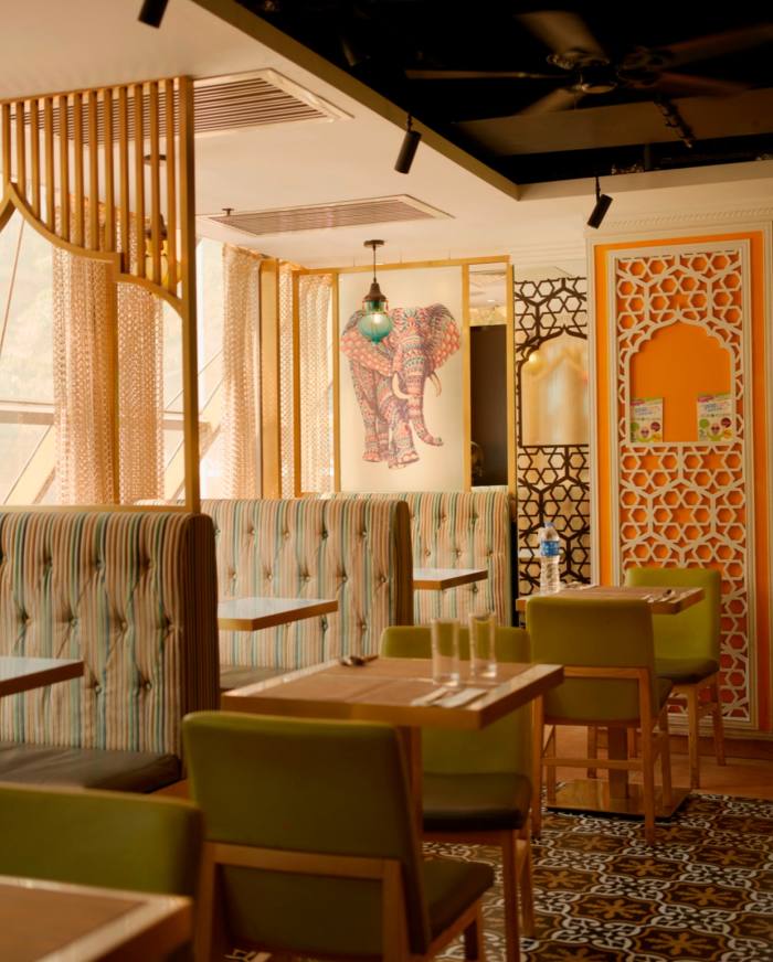 The dining space of Woodlands, with a vividly patterned brown carpet, Indian-style wooden wall ornamentation and a painting of an elephant