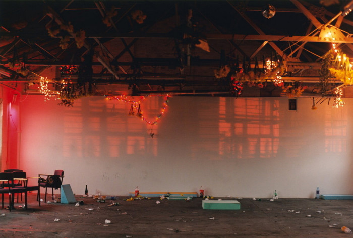 a large, orange-lit room with the paraphernalia of a party long gone