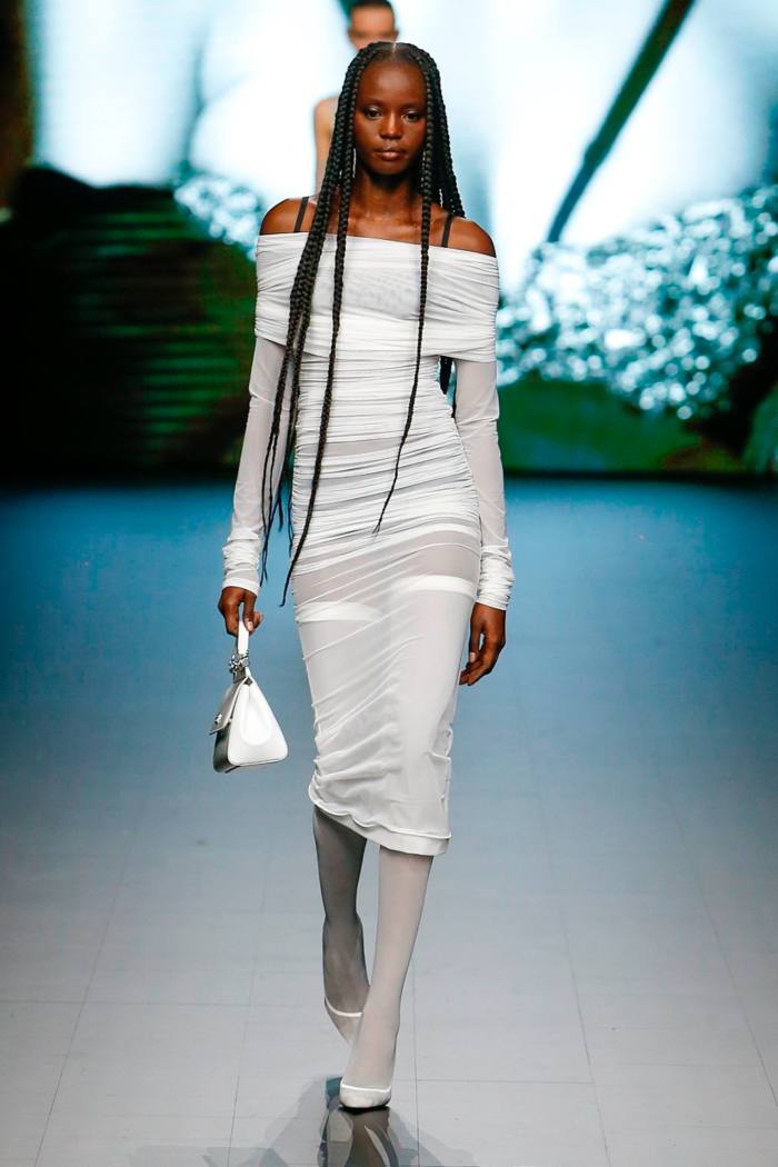 A model wears a tight-fitting white dress with white tights and shoes