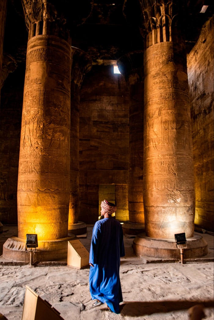 A man in Egyptian dress stands before two giant stone pillars inside a temple 