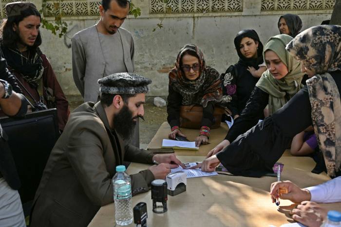 A Taliban official checks documents of people outside the passport office in Kabul, which reopened in October