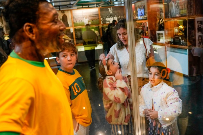 Visitors look at the life-size statue of Pele in a bright-yellow Brazil jersey, with the No. 10 stamped on the back, displayed in a glass case at the Pele Museum in Santos, Brazil, Friday, December 30 2022