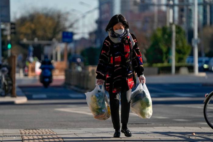 A woman wearing a face mask carries bags of groceries on a street in Beijing