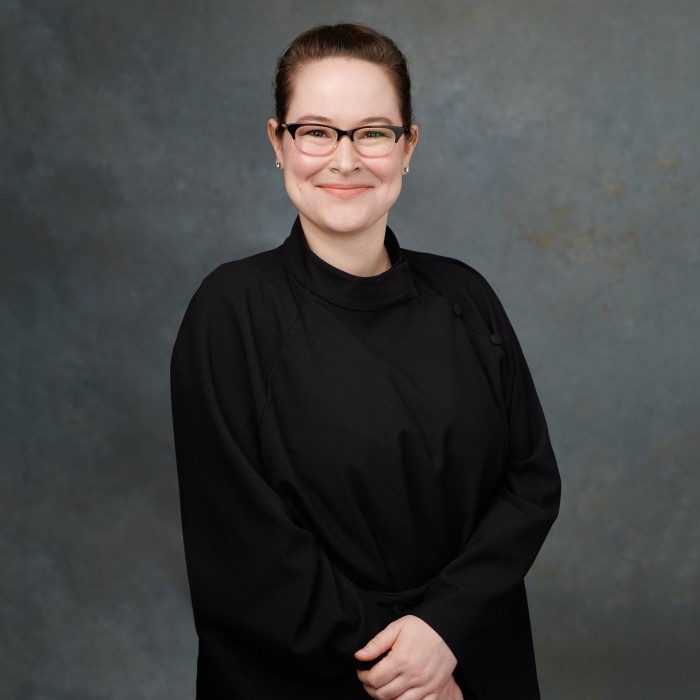 A portrait of a bespectacled female church minister in an all-black outfit