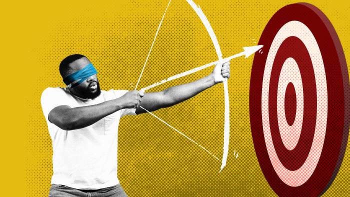 a man tries to shoot an arrow at a target while wearing a blindfold