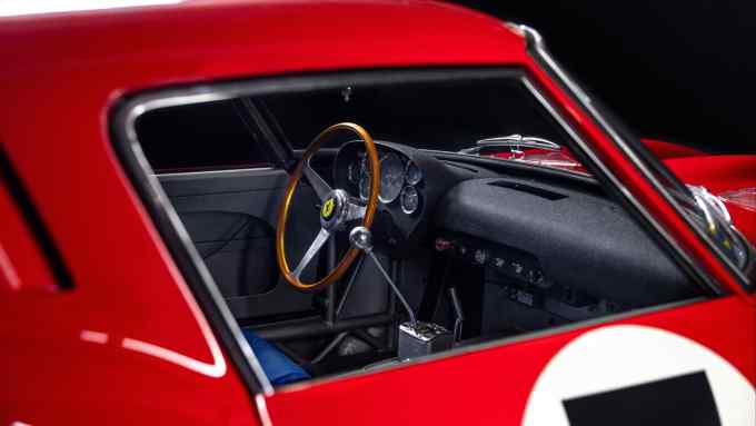 A side view of a red 1962 Ferrari, with the interior and steering wheel visible through the passenger door