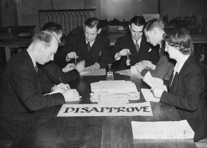 seis hombres sentados en una mesa clasificando las papeletas.  hay un suspiro marcado 'DESAPROBAR' en la mesa
