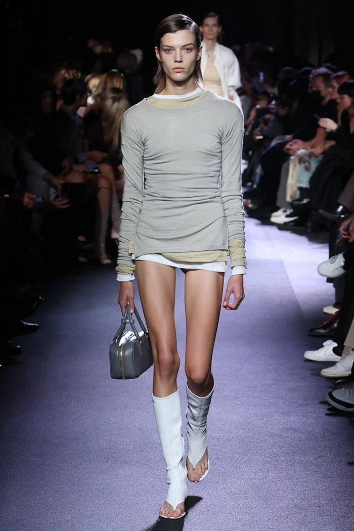 A female catwalk model wears a mini-dress with toe-revealing knee-high white boots