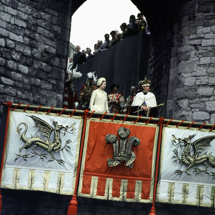 The Queen with Prince Charles at his investiture at Caernarfon Castle in 1969. They are looking down from a tower of the castle, which is hung with banners showing a dragon and the prince of wales feathers 