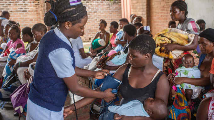 A nurse takes the blood pressures of a woman as she waits with an infant at Ndirande Health Centre in Blantyre on February 21, 2018., prior to the launch of a Typhoid Fever vaccination campaign by Malawi Liverpool Welcome Trust. Some 23000 children are being targetted for vaccination during the campaign period. / AFP PHOTO / Amos Gumulira (Photo credit should read AMOS GUMULIRA/AFP/Getty Images)