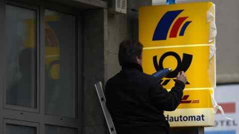 A worker puts finishing touches to an information board for a branch of German postal service Deutsche Post, its logistics unit DHL and a cashpoint of the Postbank in Berlin, April 28, 2015. Deutsche Bank, Germany's biggest lender, unveiled on April 27, 2015 details of a huge strategic shake-up in which it will rid itself of its Postbank unit and massively curb costs.     AFP PHOTO / TOBIAS SCHWARZ        (Photo credit should read TOBIAS SCHWARZ/AFP/Getty Images)
